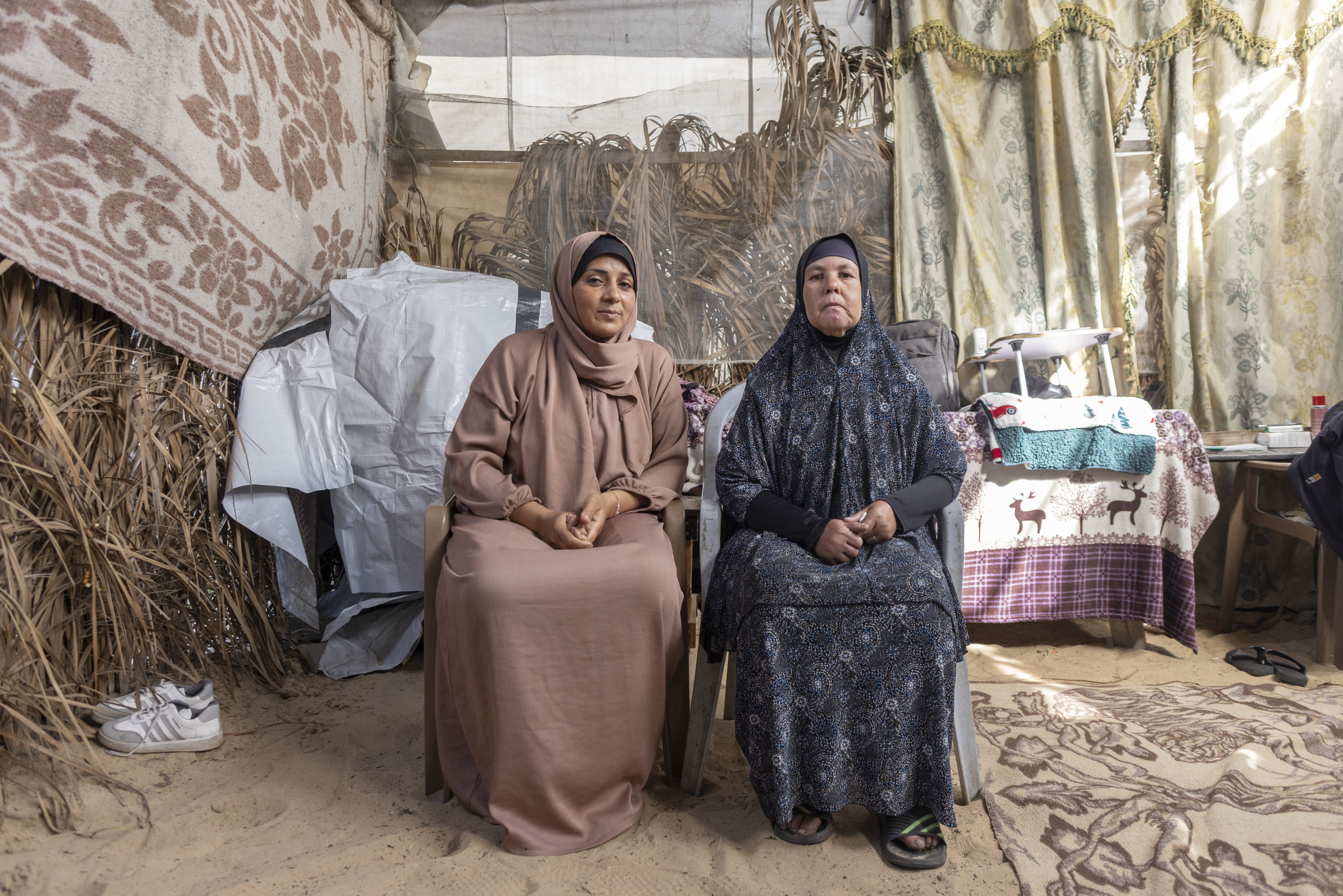 Two palestinian women sit outside their tent in gaza.