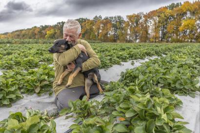 Ukrainian man kneels in agricultural scene embracing his dog.