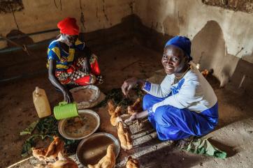 32 year old okukuru zubeda (in blue), along with another member of the embasi business group, feeds her group's chickens.