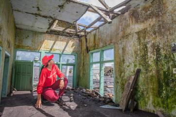 Woman in flood-damaged house inspects damaged roof.