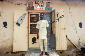 An individual stands in front of the entry to a barber school. 