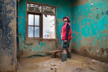 A person standing inside a mud flooded home.