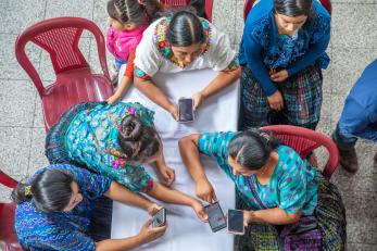 Adults sit at a table using mobile devices.