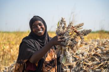 Sudanese woman poses with her sorghum harvest in celebration of a successful growing season.