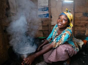 A person cooking in a one room hut.