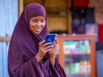 Kenyan woman working on her mobile phone in front of shop.